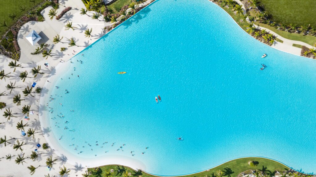 Top-down aerial view of a Crystal Lagoons amenity surrounded by palm trees and white sand beaches
