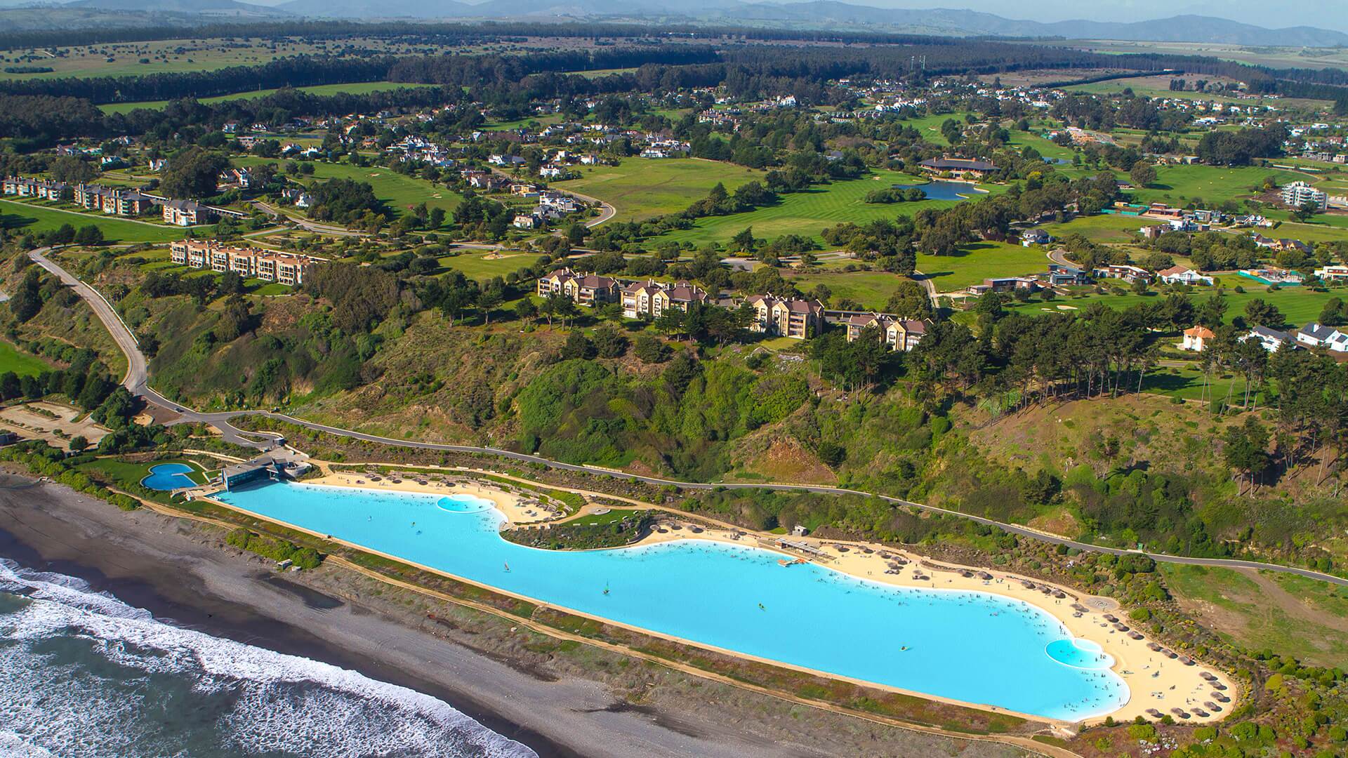 Elevated view of a Crystal Lagoons project with beach areas, amenities and surrounding buildings