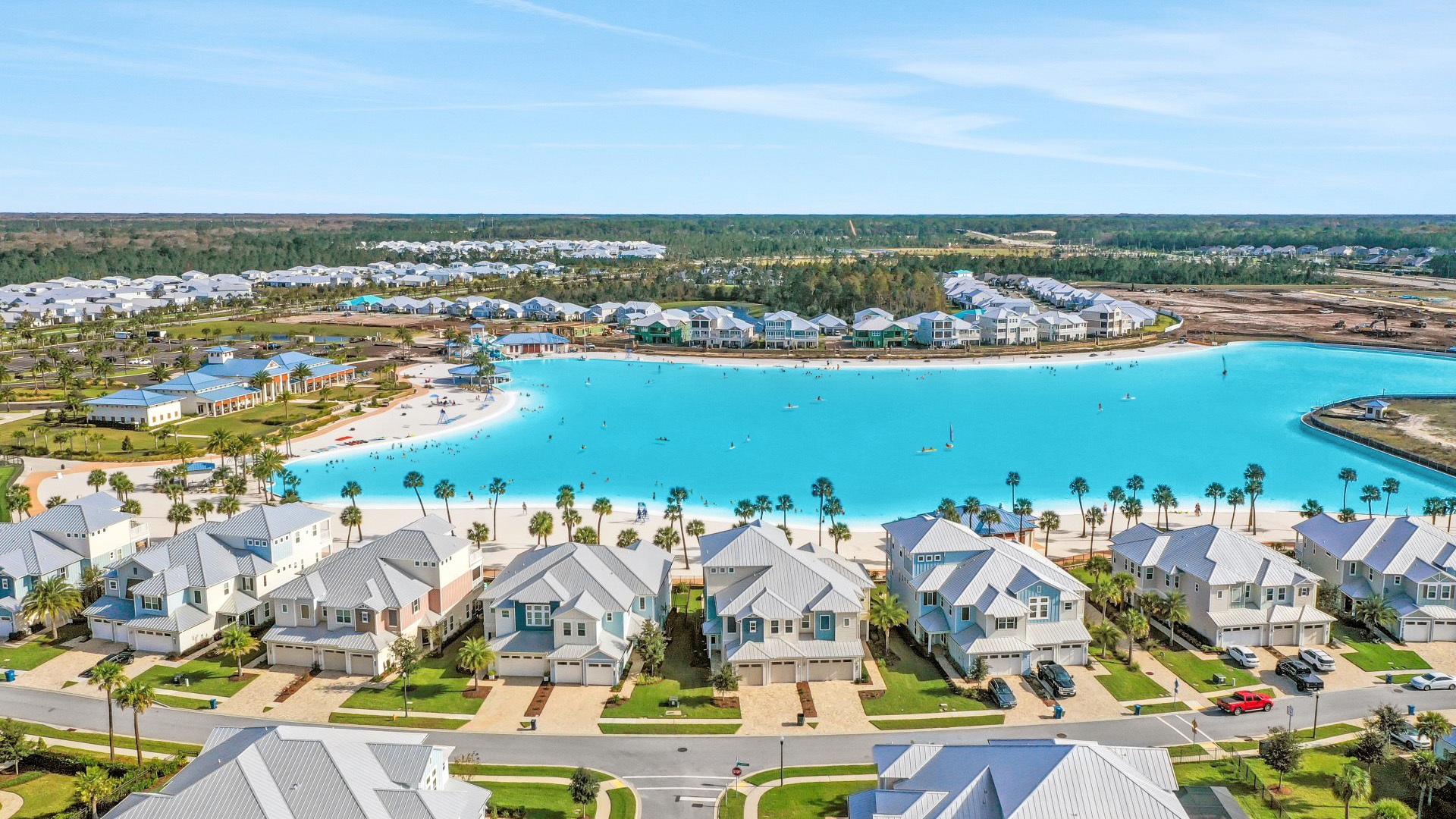 Aerial view of a residential community with white vacation homes built around a turquoise Crystal Lagoons amenity