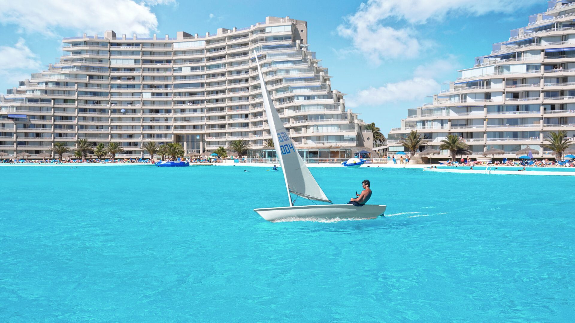Sailboat gliding on the turquoise lagoon at San Alfonso del Mar, Chile, in front of white terraced residential buildings