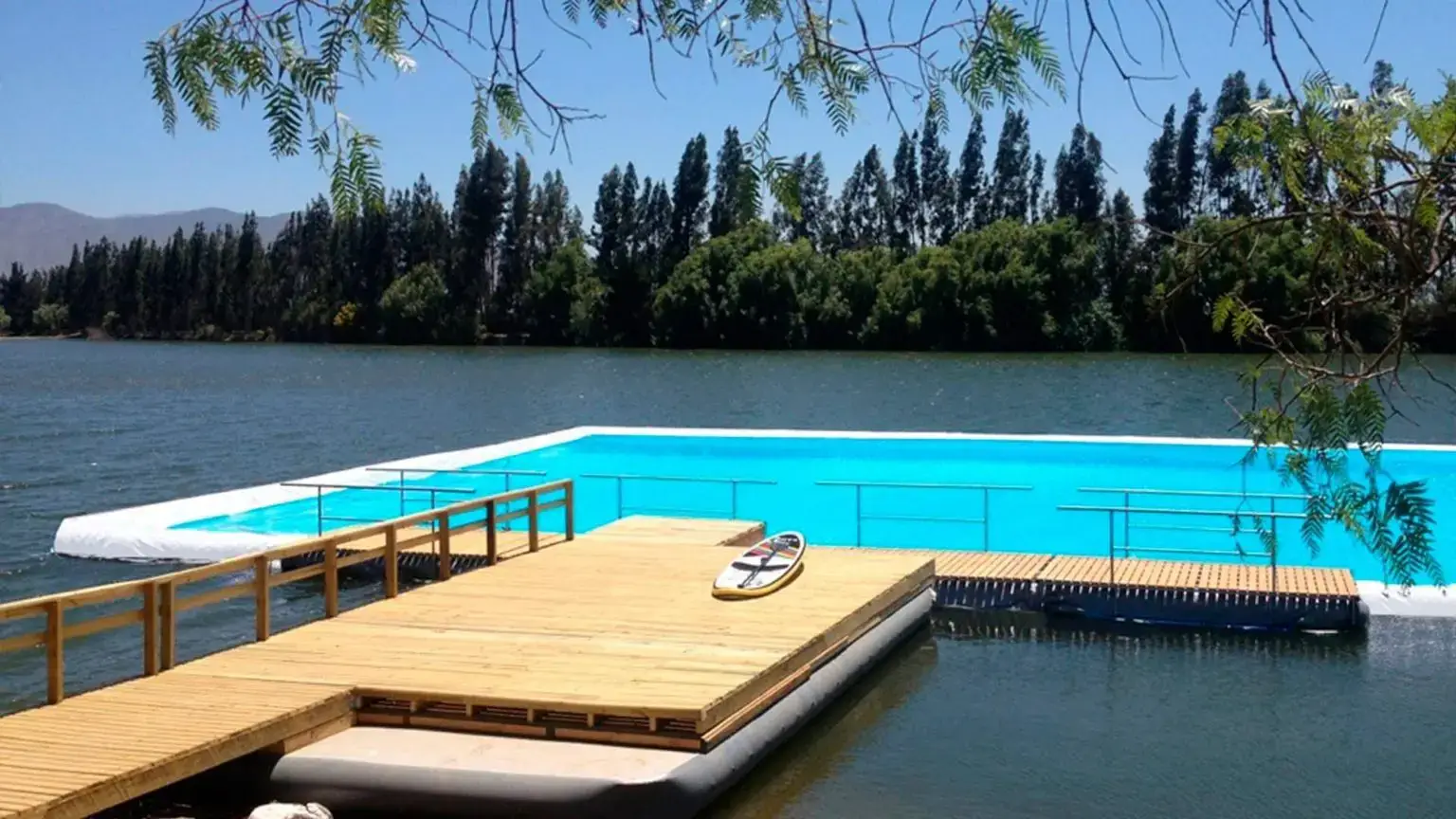 Floating turquoise lagoon with wooden deck built inside a natural lake, surrounded by trees