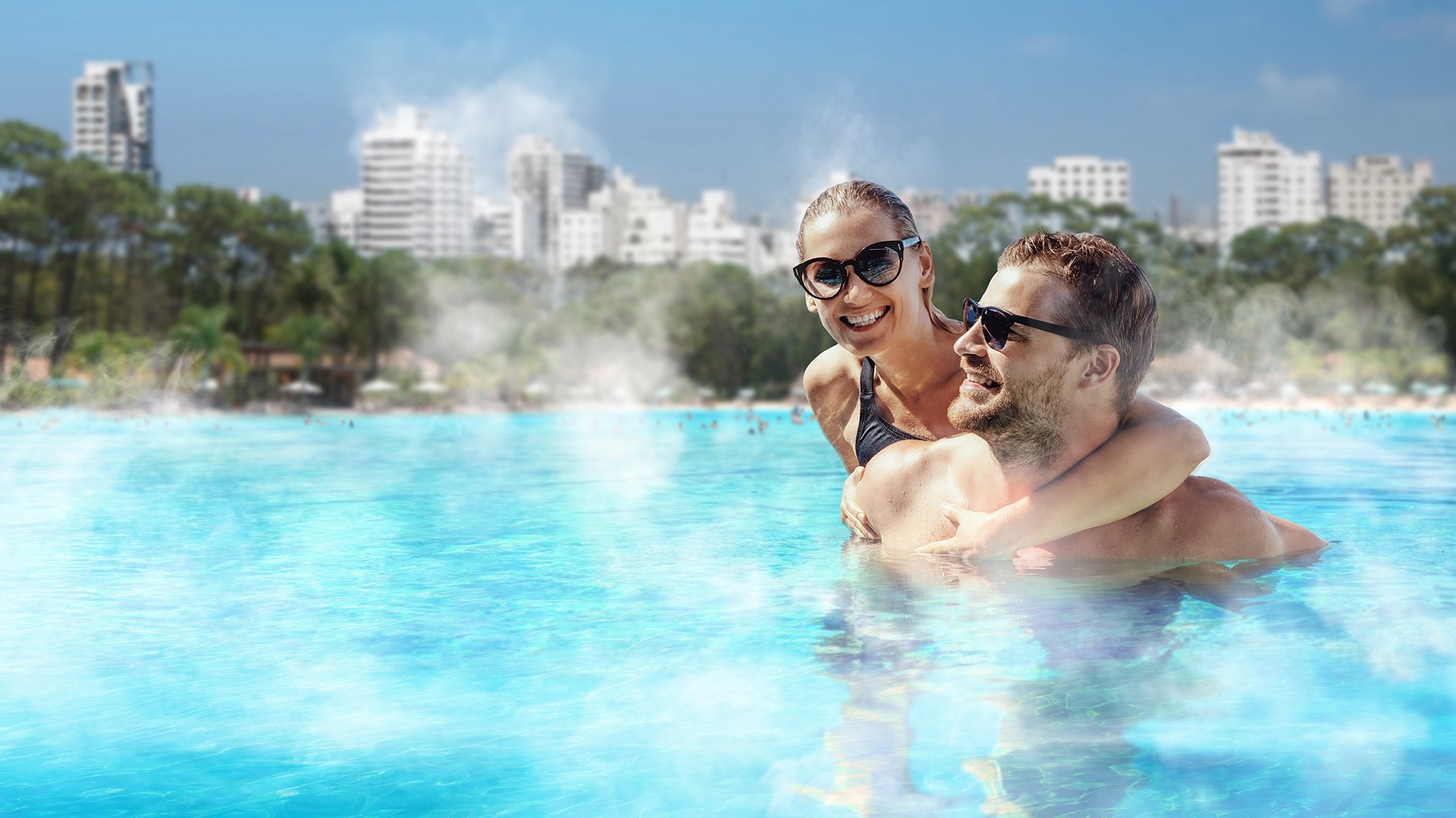 Couple in the warm steaming water of an eco-heated lagoon by Crystal Lagoons™ with city skyline behind