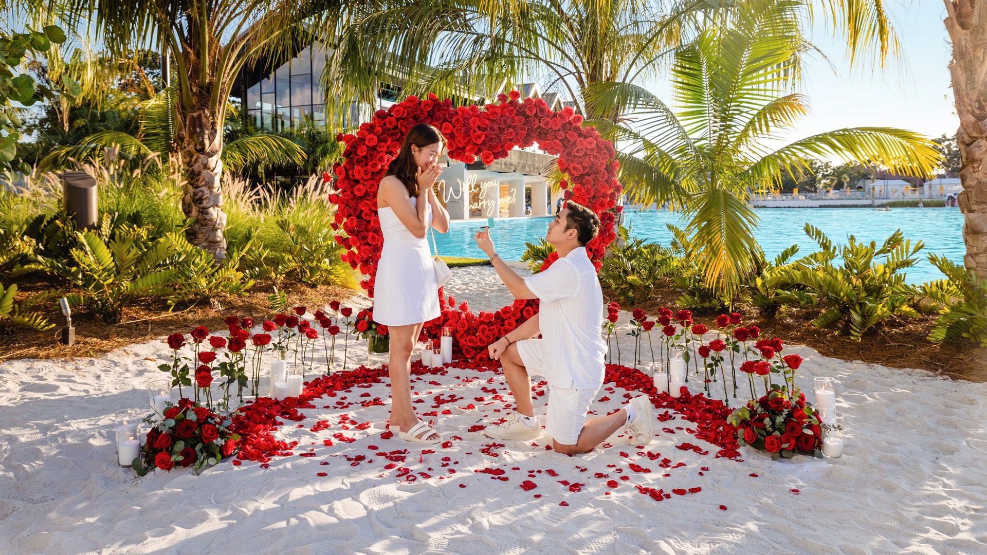 Marriage proposal under a heart-shaped rose arch on the beach of a Crystal Lagoons amenity