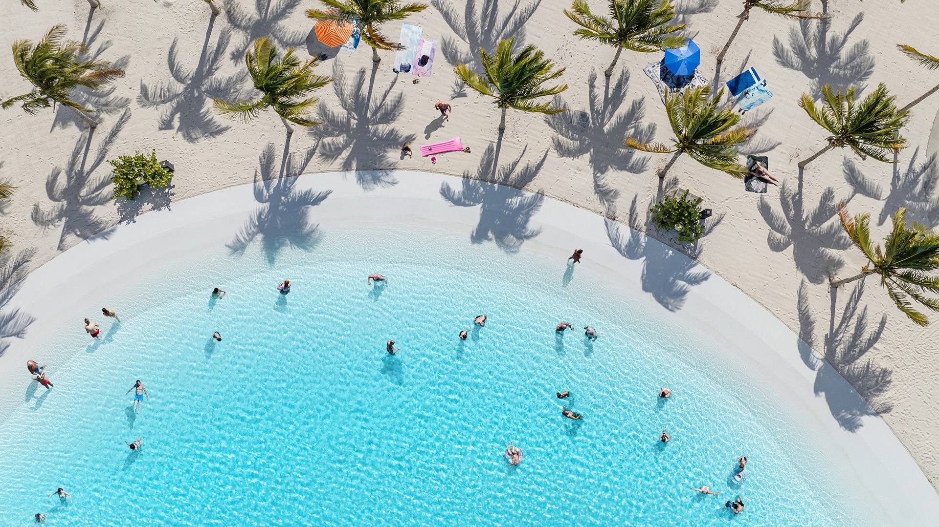 Aerial view of swimmers in the turquoise water and white sand beach of a Lagoon by Crystal Lagoons