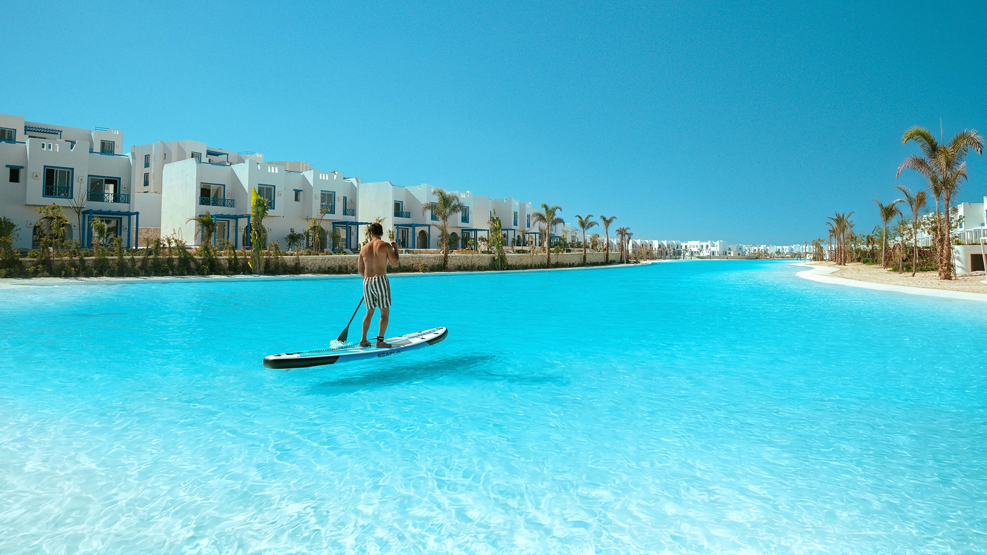 Crystal Lagoons lagoon at Mountain View Ras El Hekma with white villas and palm trees along the Mountain View Ras El Hekma lagoon shoreline, Egypt's North Coast