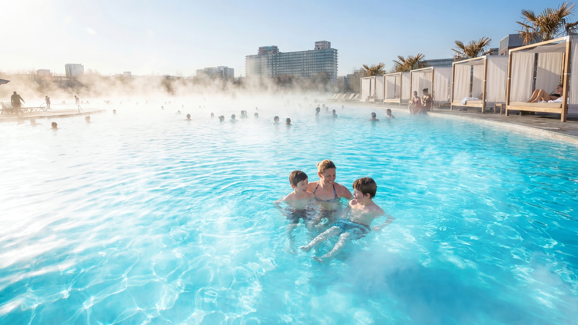 Familia feliz jugando en el agua turquesa tibia de una laguna eco-calefaccionada de Crystal Lagoons, 37°C todo el año